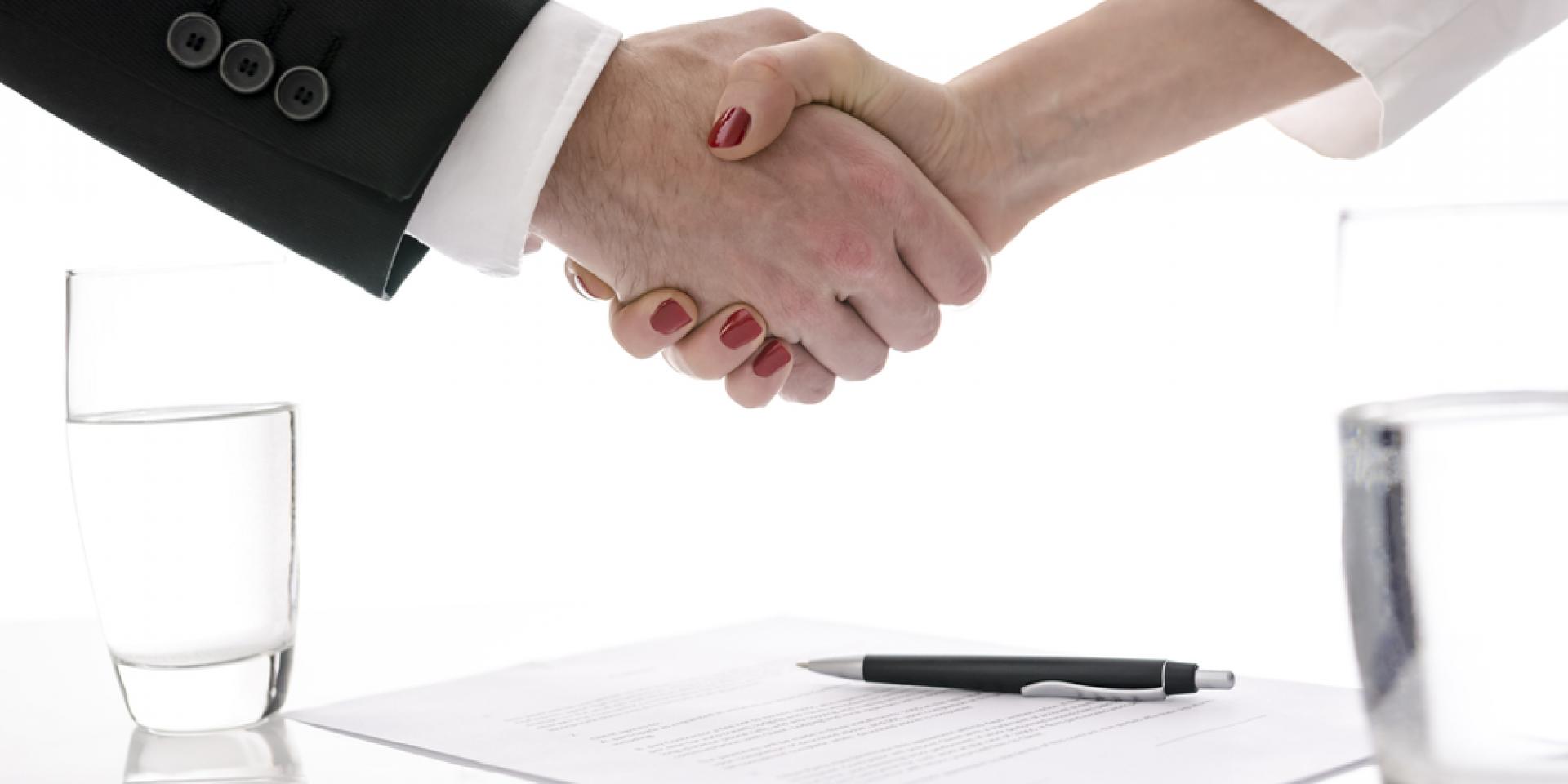Man and woman shaking hands above table with signed contract.
