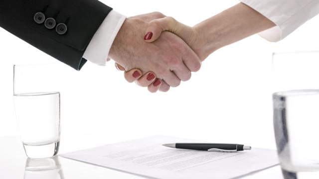 Man and woman shaking hands above table with signed contract.