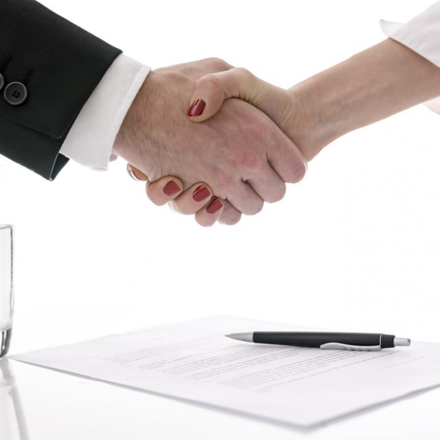 Man and woman shaking hands above table with signed contract.