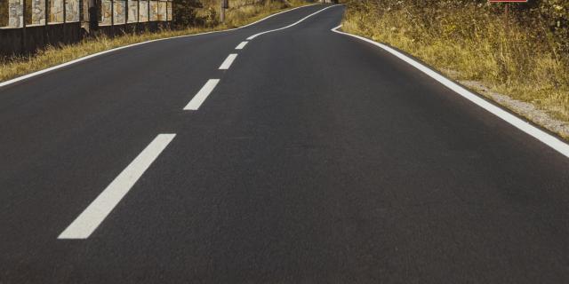 A vertical shot of an empty asphalt road through mountains under a cloudy sky