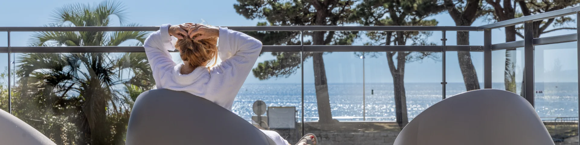 Eine Frau, die sich mit Blick auf das Meer im Teeraum des Thalasso-Relais sonnt.