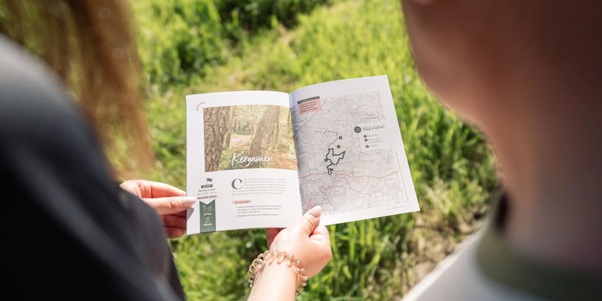 Two walkers looking at the Carnet du Promeneur page about the walk in the Bois de Kergaouen in Bénodet