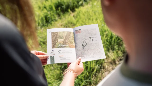 Deux promeneurs regardant la Carnet du Promeneur à la page concernant la balade dans le Bois de Kergaouen à Bénodet