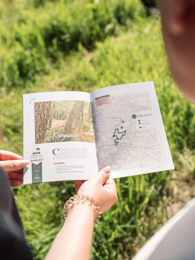 Two walkers looking at the Carnet du Promeneur page about the walk in the Bois de Kergaouen in Bénodet