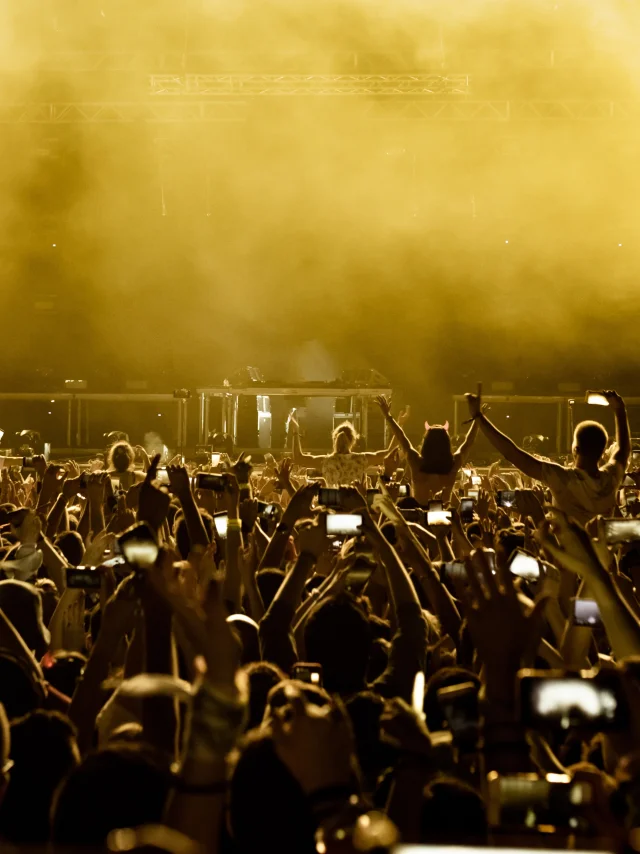 Vista trasera de aficionados entusiasmados divirtiéndose en un festival de música y tomando fotos del escenario con sus teléfonos inteligentes.  Espacio de copia.