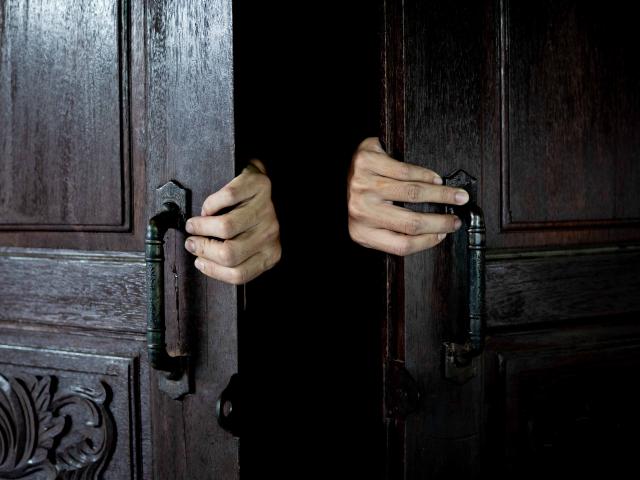 Hands open the wooden door from the inside of the dark room.