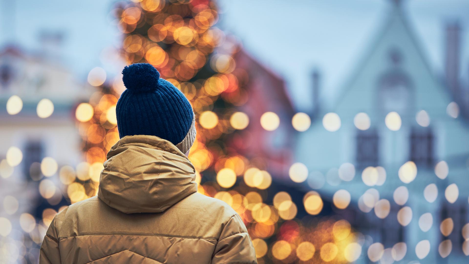 Rear view of man in warm clothing during walk in city. Christmas tree and decoration in Old Town in Tallinn, Estonia.