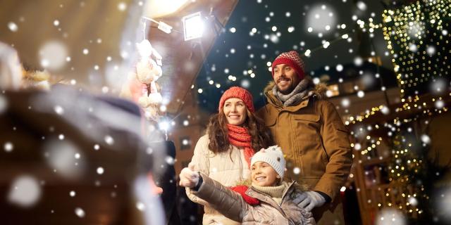 family, winter holidays and celebration concept - happy mother, father and little daughter at christmas market on town hall square in tallinn, estonia over snow