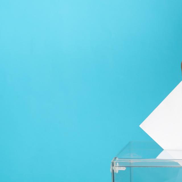 Man putting ballot into voting box on blue background