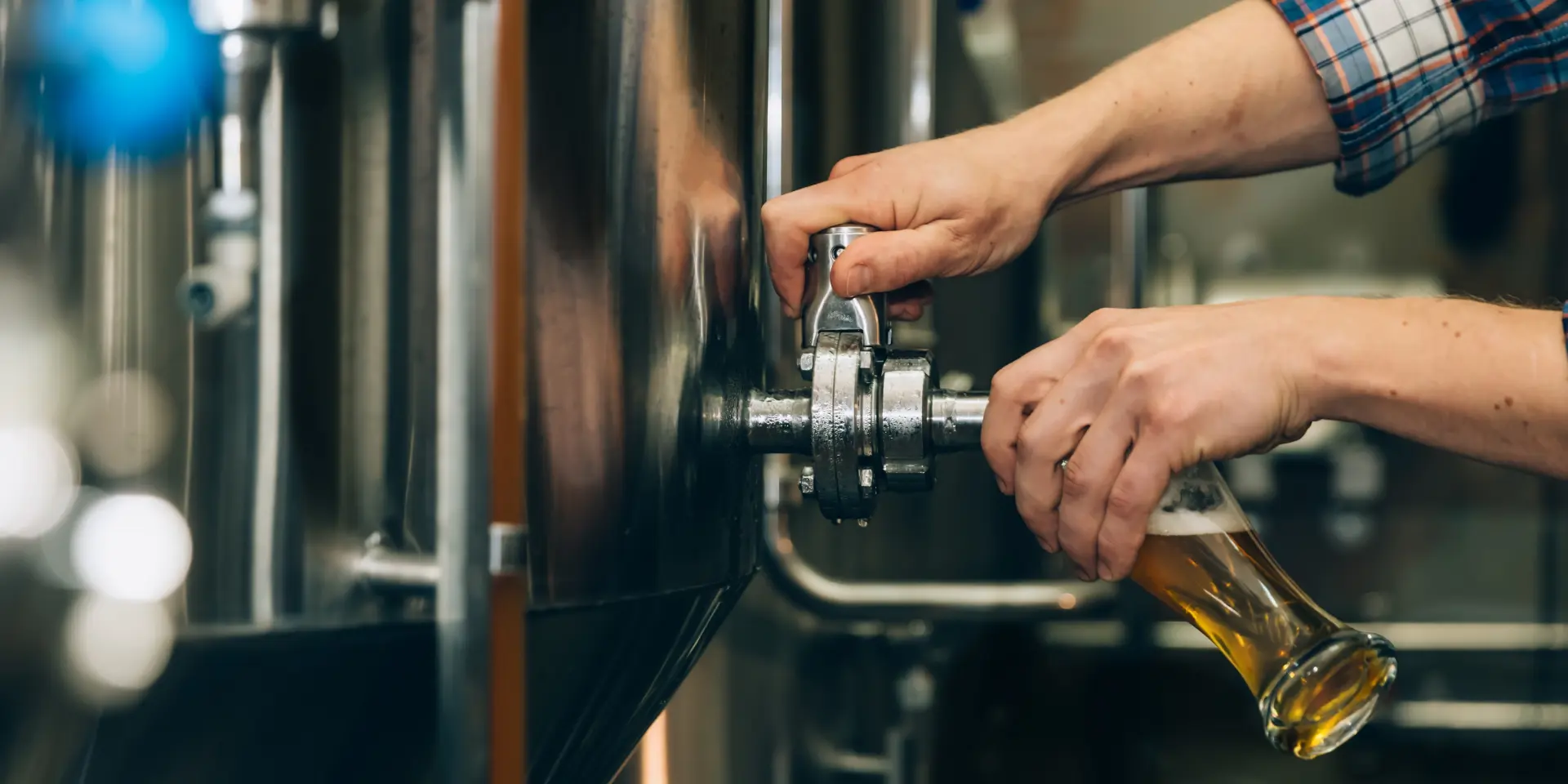 Brewer filling beer in glass from tank at brewery