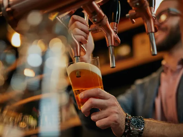 Tattooed caucasian barman pouring beer while standing in pub.