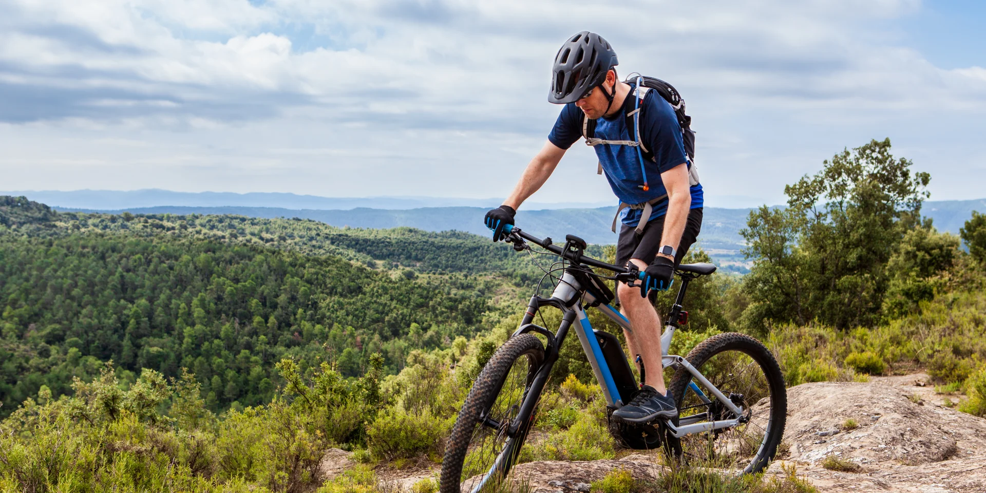 Mannelijke mountainbiker balanceert zijn ebike op een rots, mooi landschap op de achtergrond