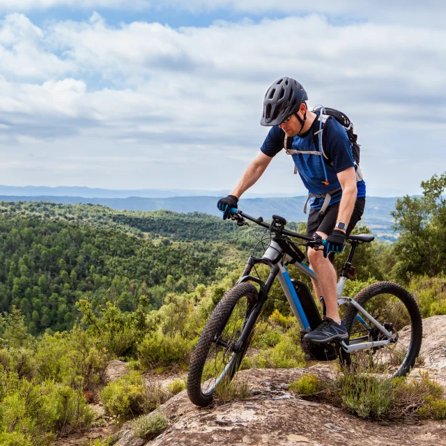 Mannelijke mountainbiker balanceert zijn ebike op een rots, mooi landschap op de achtergrond