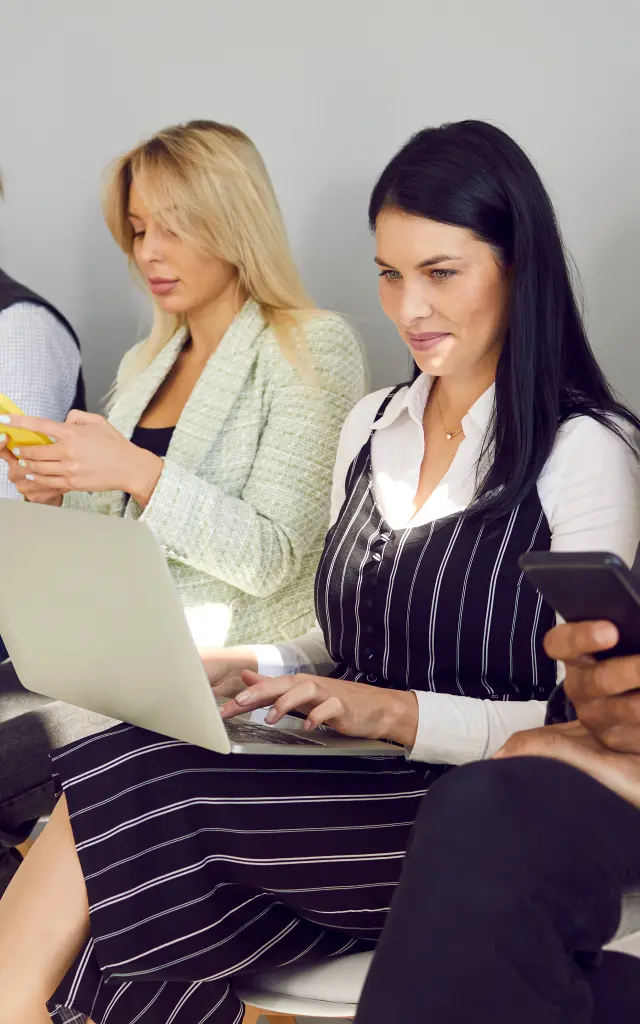 Different diverse multiethnic mixed race business people in smart casual clothes holding laptops, using cellphones, reading papers, documents, CVs and resumes while waiting in line for job interview