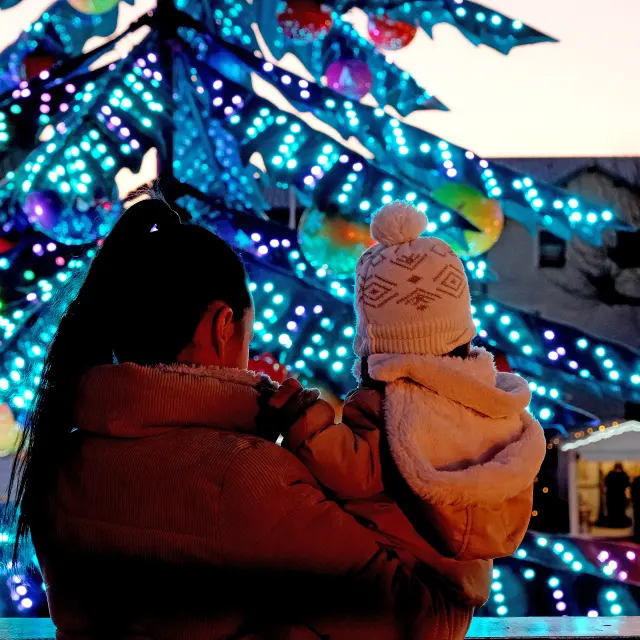 Mère et enfant admirant le grand sapin illuminé du marché de Noël de Châtelaillon-Plage au crépuscule, en Charente-Maritime sur la côte Atlantique.