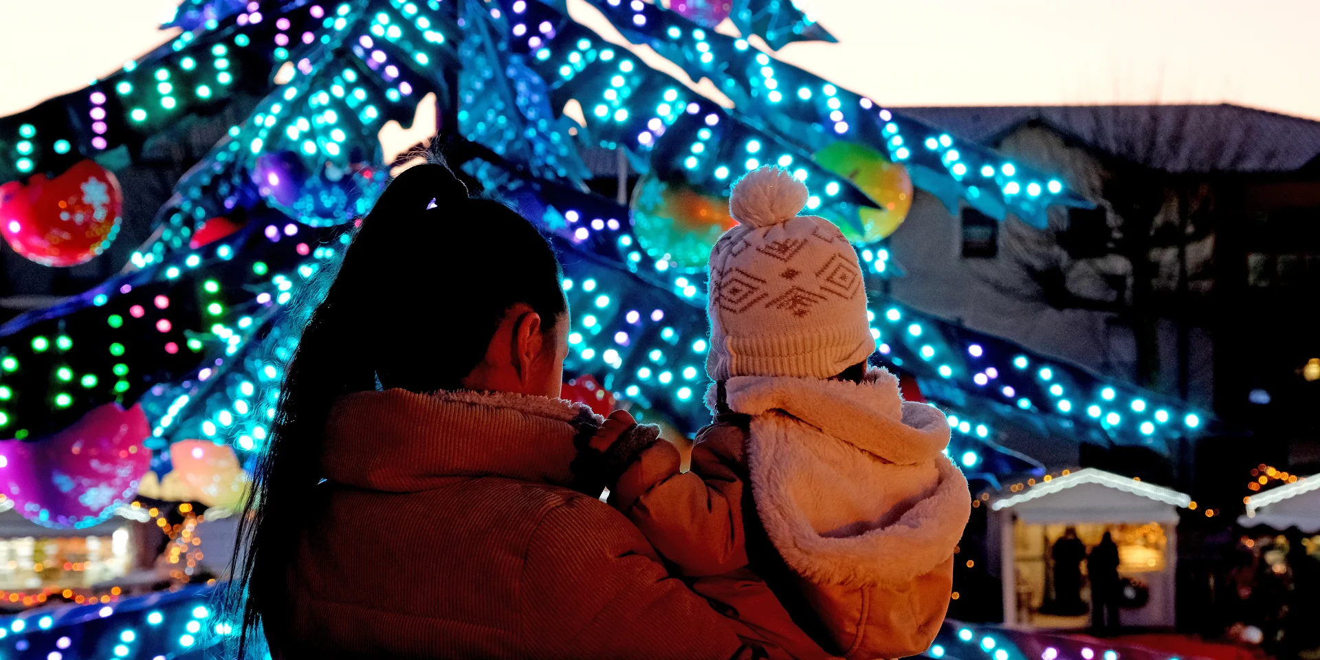 Mère et enfant admirant le grand sapin illuminé du marché de Noël de Châtelaillon-Plage au crépuscule, en Charente-Maritime sur la côte Atlantique.