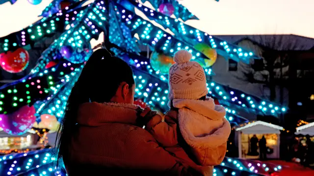 Mère et enfant admirant le grand sapin illuminé du marché de Noël de Châtelaillon-Plage au crépuscule, en Charente-Maritime sur la côte Atlantique.