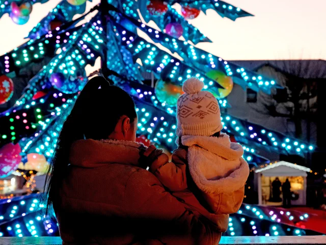 Mère et enfant admirant le grand sapin illuminé du marché de Noël de Châtelaillon-Plage au crépuscule, en Charente-Maritime sur la côte Atlantique.
