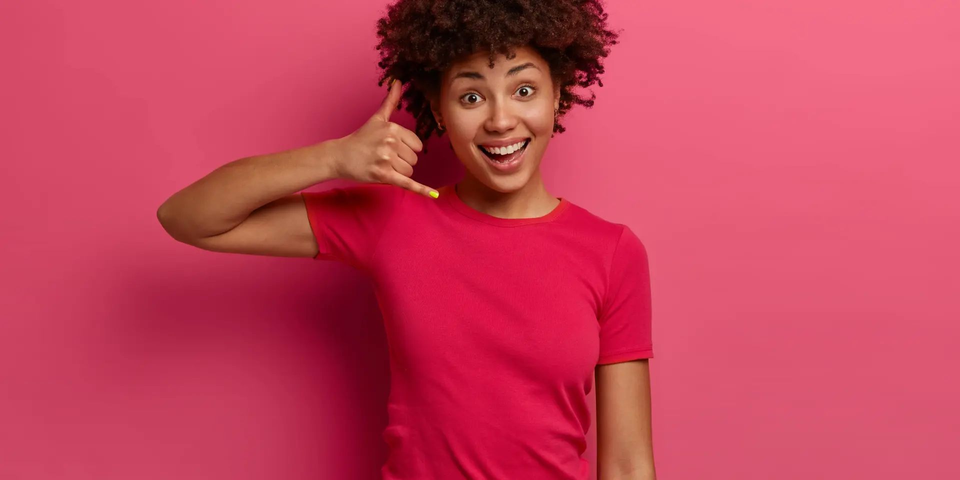 Jeune femme souriante mimant un appel téléphonique avec sa main droite