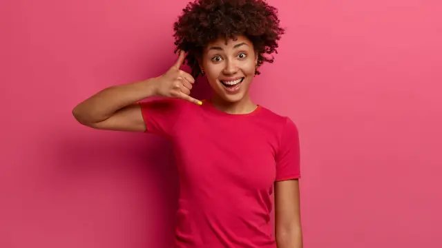 Jeune femme souriante mimant un appel téléphonique avec sa main droite