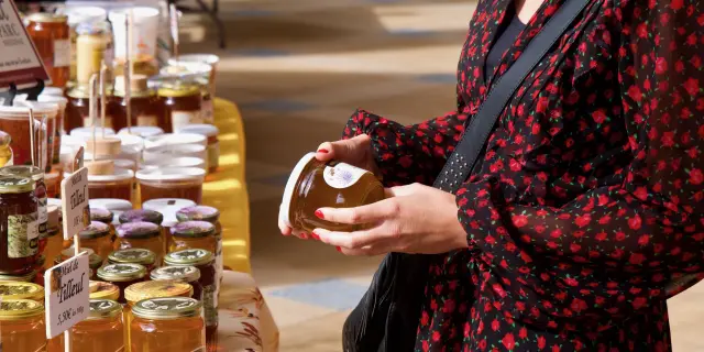 Jeune femme tenant un pot de miel lors d'un marché du terroir sous la galerie thermale de Contrexéville
