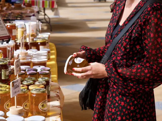 Jeune femme tenant un pot de miel lors d'un marché du terroir sous la galerie thermale de Contrexéville