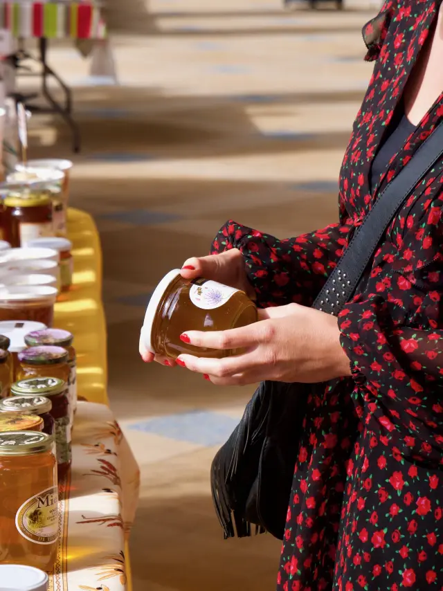 Jeune femme tenant un pot de miel lors d'un marché du terroir sous la galerie thermale de Contrexéville