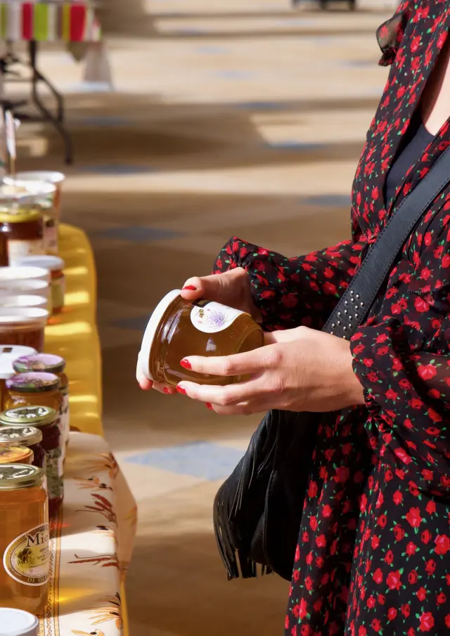 Jeune femme tenant un pot de miel lors d'un marché du terroir sous la galerie thermale de Contrexéville