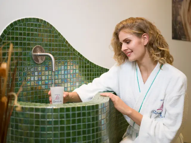 Jeune femme en peignoir prenant l'eau à la source à l'intérieur des Thermes de Contrexéville
