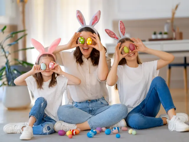 Happy holiday. Mother and her daughters with painting eggs. Family celebrating Easter. Cute little children girls are wearing bunny ears.