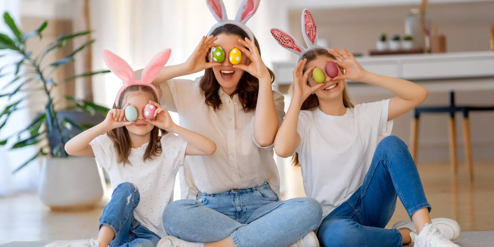 Happy holiday. Mother and her daughters with painting eggs. Family celebrating Easter. Cute little children girls are wearing bunny ears.