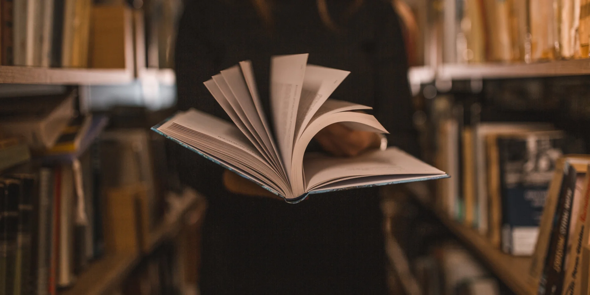 An unrecognizable librarian holds a book in her hands and turns the pages