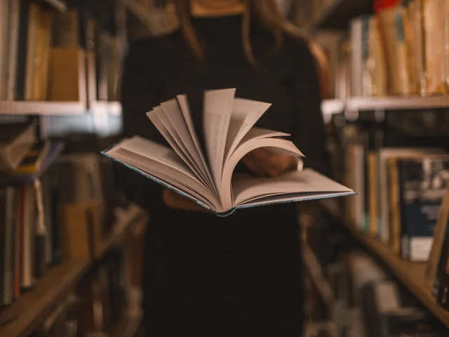 An unrecognizable librarian holds a book in her hands and turns the pages