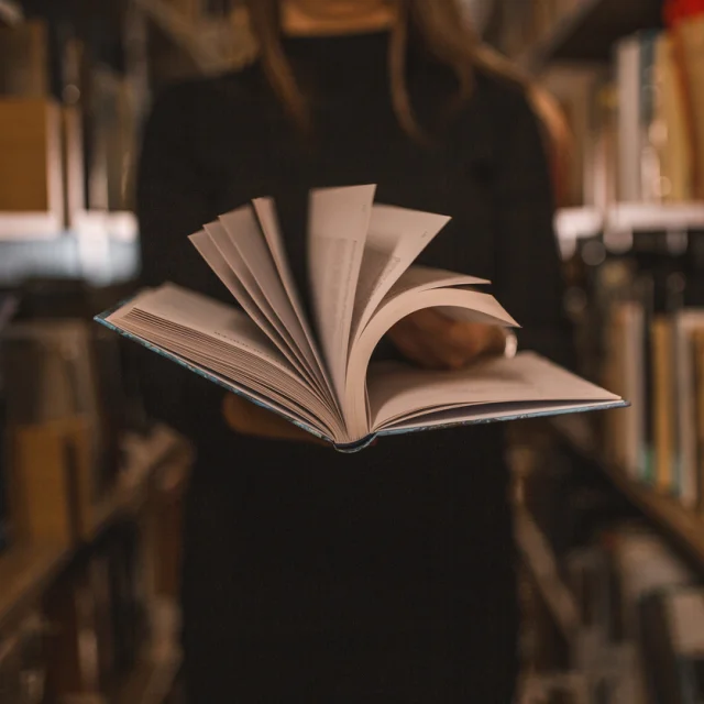 An unrecognizable librarian holds a book in her hands and turns the pages
