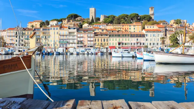 Vue sur le Vieux-Port de Cannes et le quartier du Suquet au printemps, avec bateaux traditionnels et reflets sur la mer
