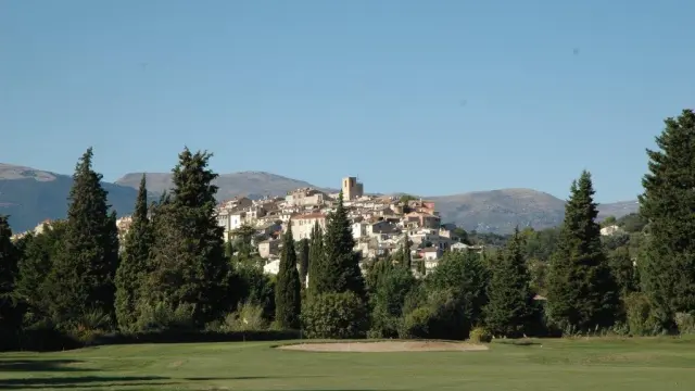 Vue panoramique sur le village perché de Biot entouré de collines verdoyantes et de montagnes en arrière-plan.