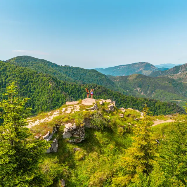 Deux randonneurs sur un promontoire rocheux au Pays des Paillons, face à un panorama de montagnes verdoyantes.