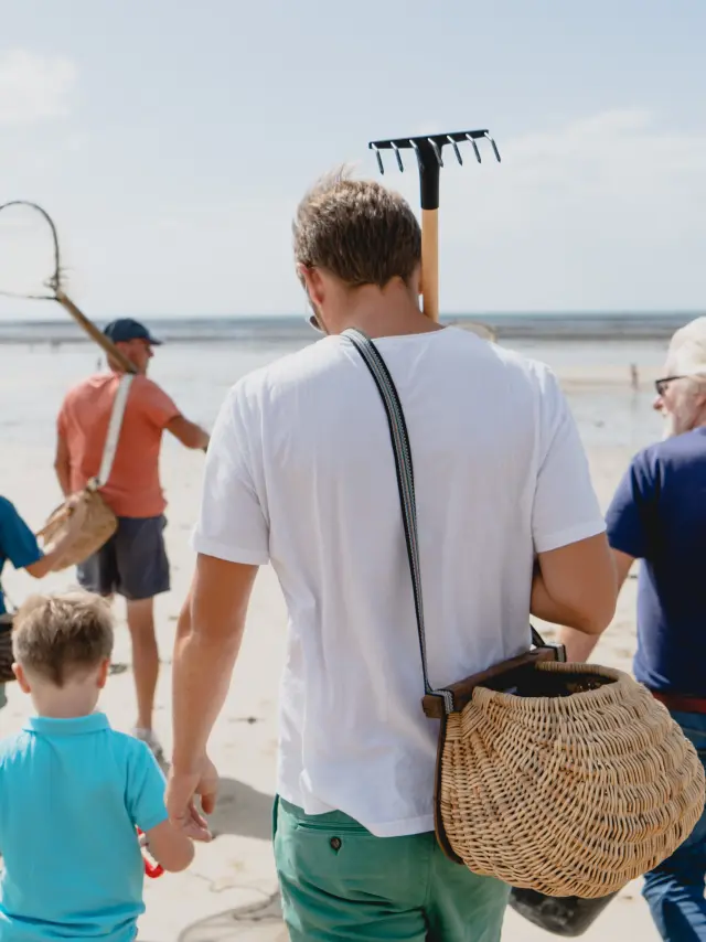 Eine Familie geht am Strand mit Werkzeugen zum Sammeln von Muscheln