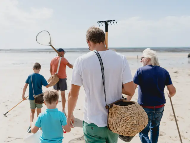 Une famille marchant sur la plage avec des outils pour chercher des coquillages