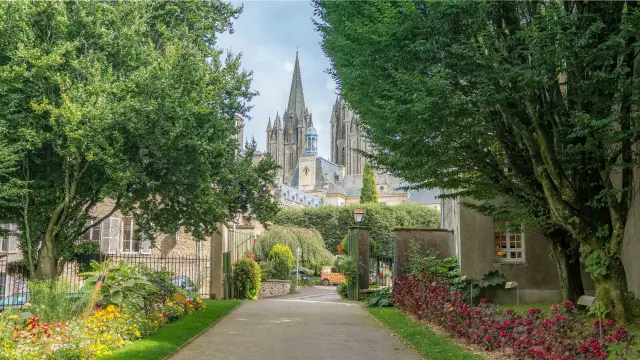 Allée bordée de fleurs et d'arbres menant à une cathédrale gothique avec une flèche pointue