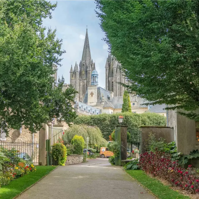 Allée bordée de fleurs et d'arbres menant à une cathédrale gothique avec une flèche pointue