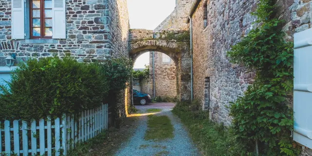 Allée pavée menant à une arche en pierre entre deux bâtiments anciens