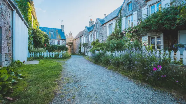 Rue pavée bordée de maisons en pierre avec des jardins bien entretenus