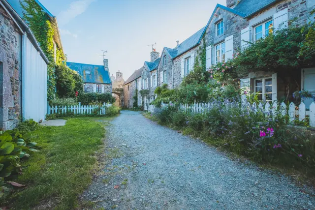 Rue pavée bordée de maisons en pierre avec des jardins bien entretenus
