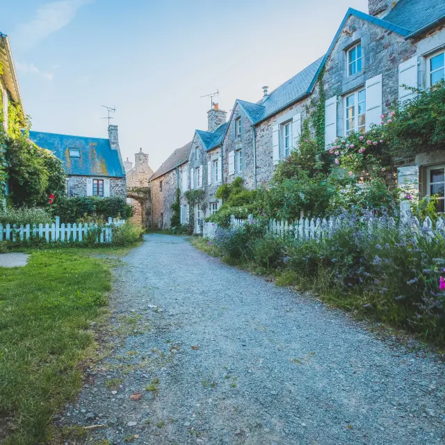 Rue pavée bordée de maisons en pierre avec des jardins bien entretenus