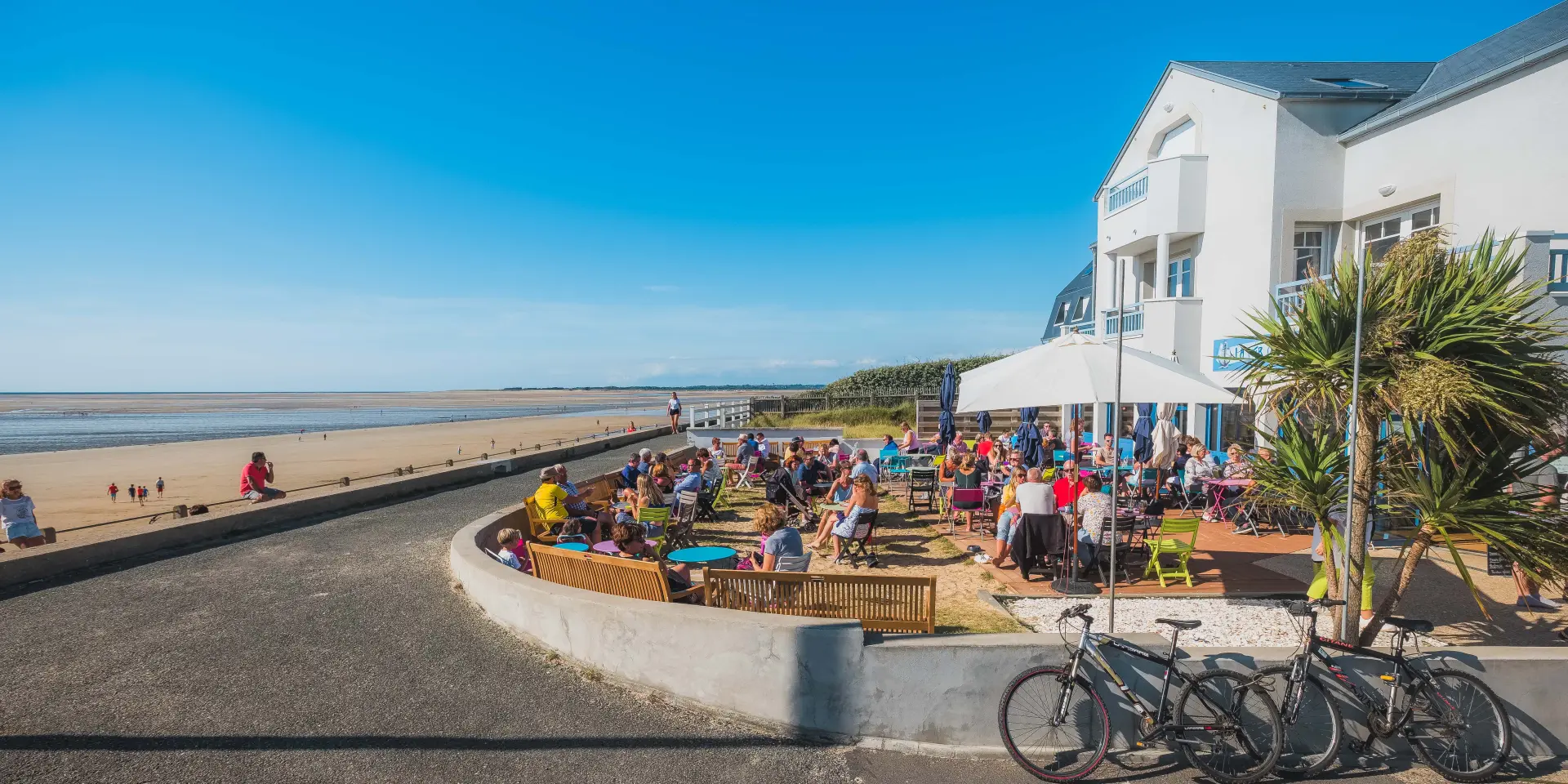 Terrasse de café bondée en bord de plage avec des gens assis et des vélos garés