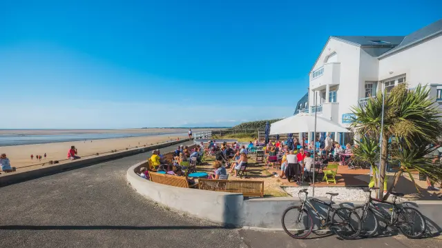 Terrasse de café bondée en bord de plage avec des gens assis et des vélos garés
