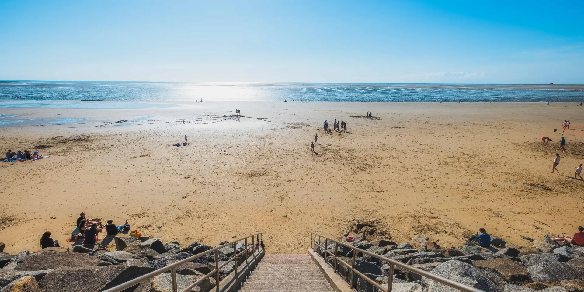 Escaliers menant à une plage de sable avec des gens se relaxant et jouant près de l'eau