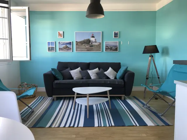 Salon avec canapé noir, table basse blanche, et murs turquoise