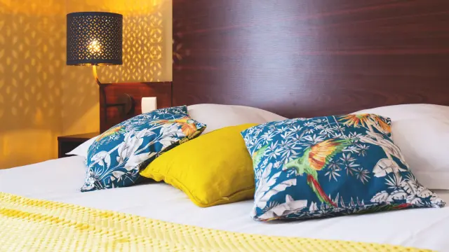 Lit d'hôtel avec couverture à motifs de vagues bleues et jaunes, sous une lumière tamisée